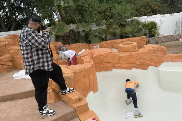 A camera operator filming the plaster crew at work inside the freshly surfaced pool